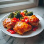 Three pieces of glazed Sheet Pan Ginger Orange Chicken Thighs served with roasted broccoli and red peppers.