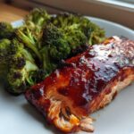 Close-up of a piece of Sheet Pan Honey Harissa Salmon with a glossy glaze next to roasted broccoli florets.
