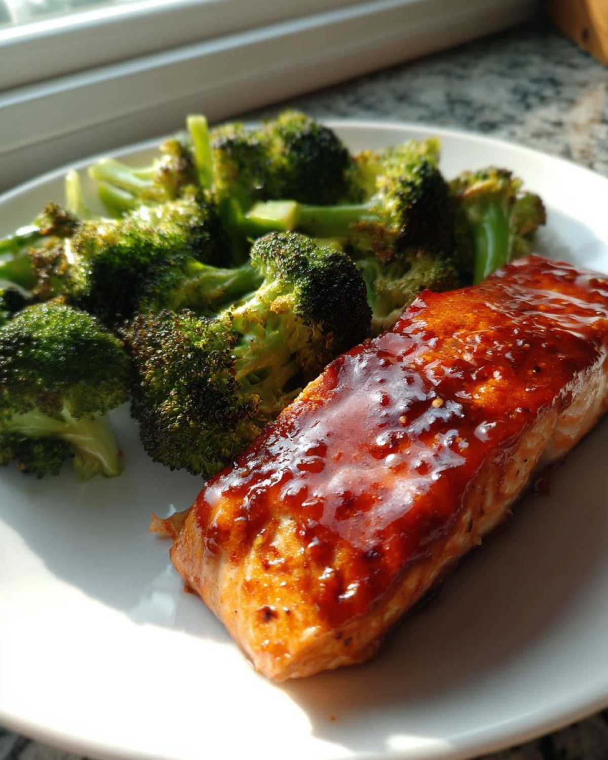 A serving of Sheet Pan Honey Harissa Salmon with roasted broccoli florets on a white plate.