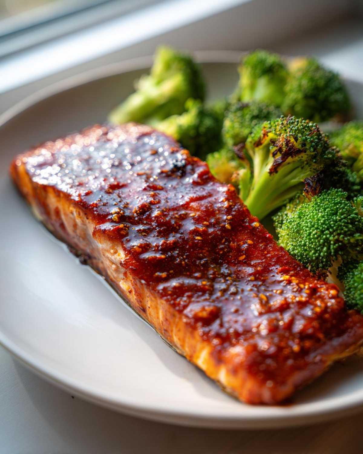 Close-up of a perfectly cooked fillet of Sheet Pan Honey Harissa Salmon topped with a rich, spicy glaze, served alongside roasted broccoli florets.
