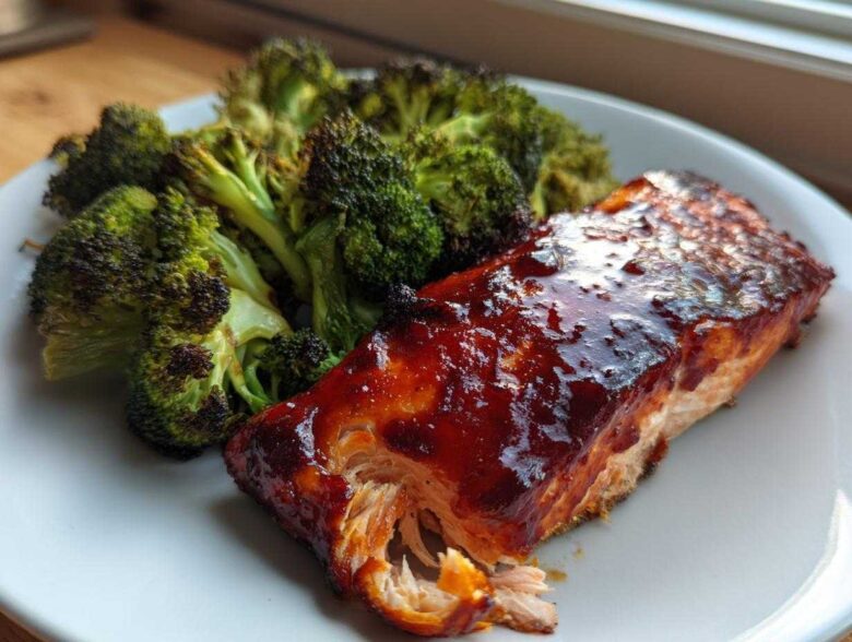 Close-up of a piece of Sheet Pan Honey Harissa Salmon with a glossy glaze next to roasted broccoli florets.