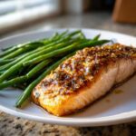 Close-up of a perfectly cooked salmon fillet topped with a whole grain honey mustard glaze, served next to bright green beans.