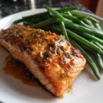 A perfectly cooked fillet of Sheet Pan Honey Mustard Salmon topped with glaze, served next to bright green beans.