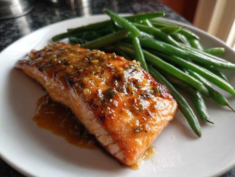 A perfectly cooked fillet of Sheet Pan Honey Mustard Salmon topped with glaze, served next to bright green beans.