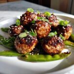 Close-up of Sheet Pan Sticky Sesame Meatballs glazed with sauce and sprinkled with sesame seeds, served over bright green snap peas.