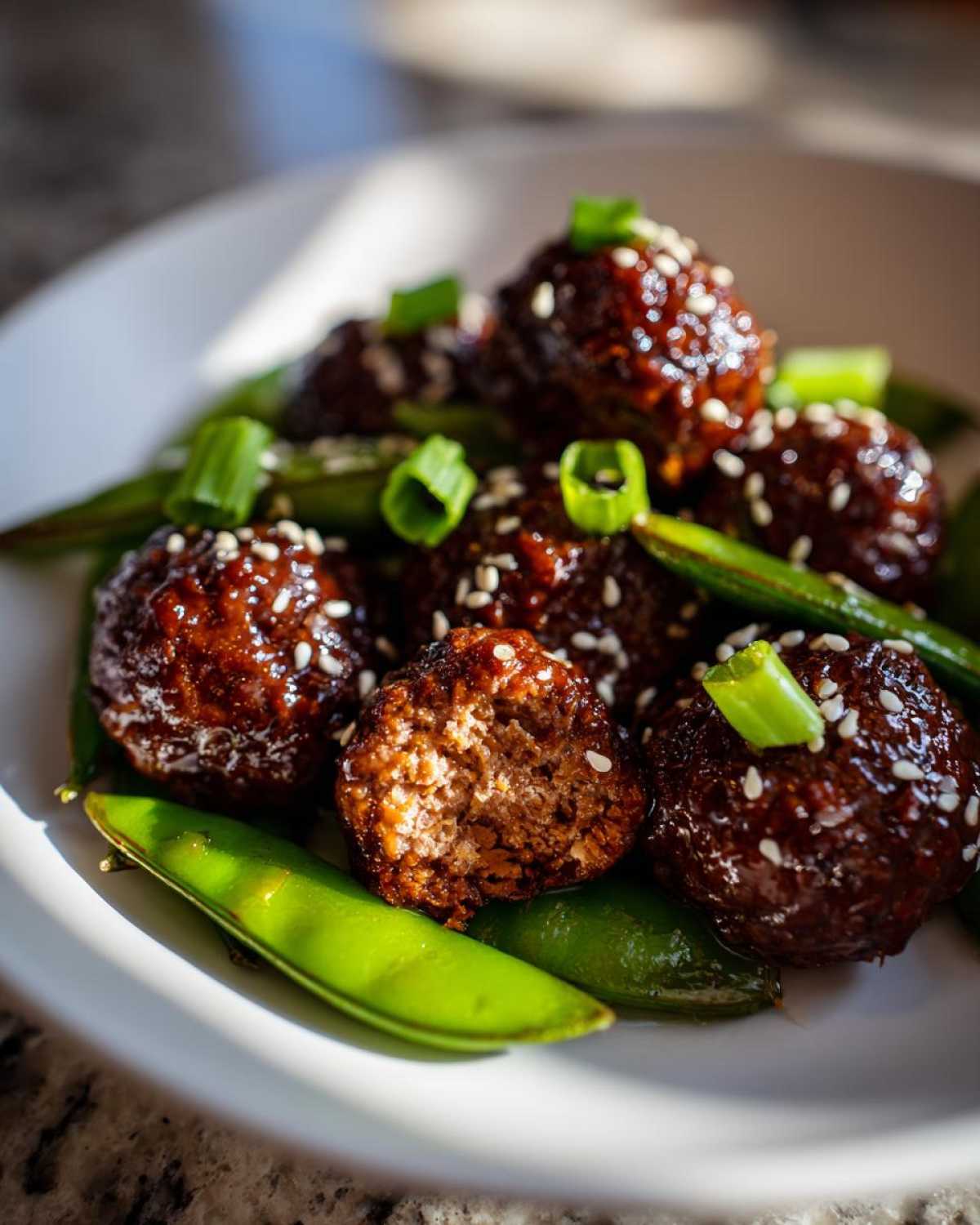 Close-up of glossy Sheet Pan Sticky Sesame Meatballs served over bright green snap peas and garnished with sesame seeds.