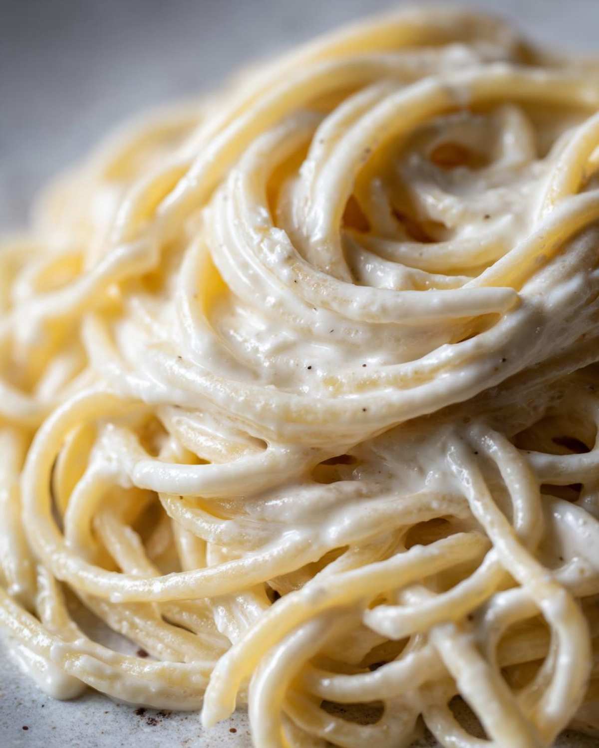 Close-up of spaghetti noodles generously coated in creamy Easy Cottage Cheese Alfredo Sauce with specks of pepper.