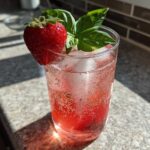 Close-up of Sparkling Strawberry Basil Lemonade garnished with a fresh strawberry and basil leaves, filled with ice.