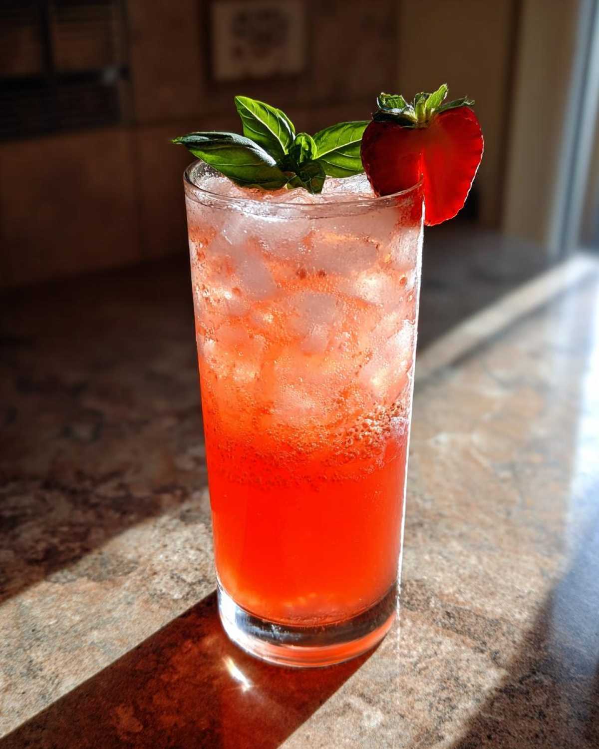 A tall glass filled with Sparkling Strawberry Basil Lemonade, ice, garnished with fresh basil and a strawberry slice.