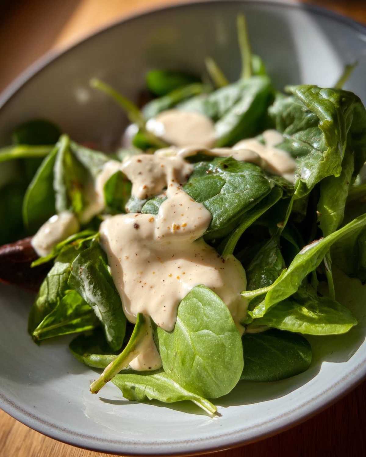 Close-up of fresh spinach leaves generously topped with Vegan Creamy Lemon Tahini Dressing.