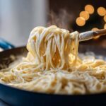 A wooden spoon lifts steaming spaghetti coated in creamy Easy Cottage Cheese Alfredo Sauce from a dark skillet.
