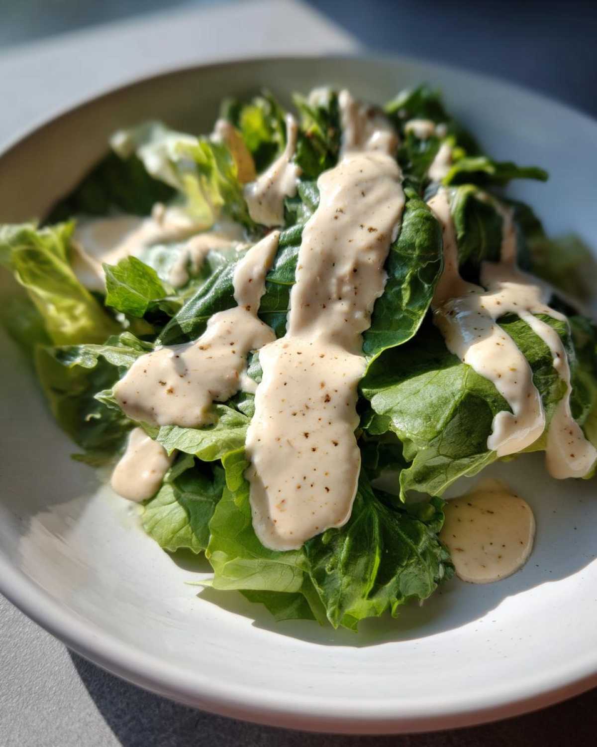 Fresh lettuce generously topped with Vegan Creamy Lemon Tahini Dressing, showing its thick texture and pepper flecks.