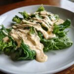 Close-up of fresh lettuce generously topped with Vegan Creamy Lemon Tahini Dressing and cracked black pepper.