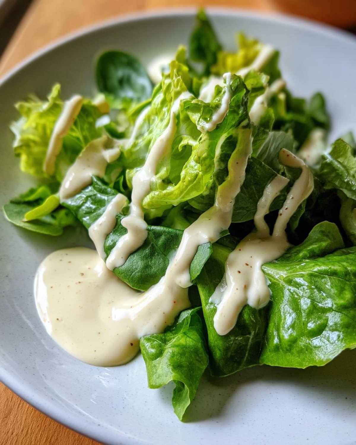 Fresh green lettuce drizzled generously with Vegan Creamy Lemon Tahini Dressing in a light gray bowl.
