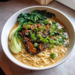 A close-up of Vegan Creamy Miso Sesame Noodle Soup topped with shiitake mushrooms, bok choy, and scallions.