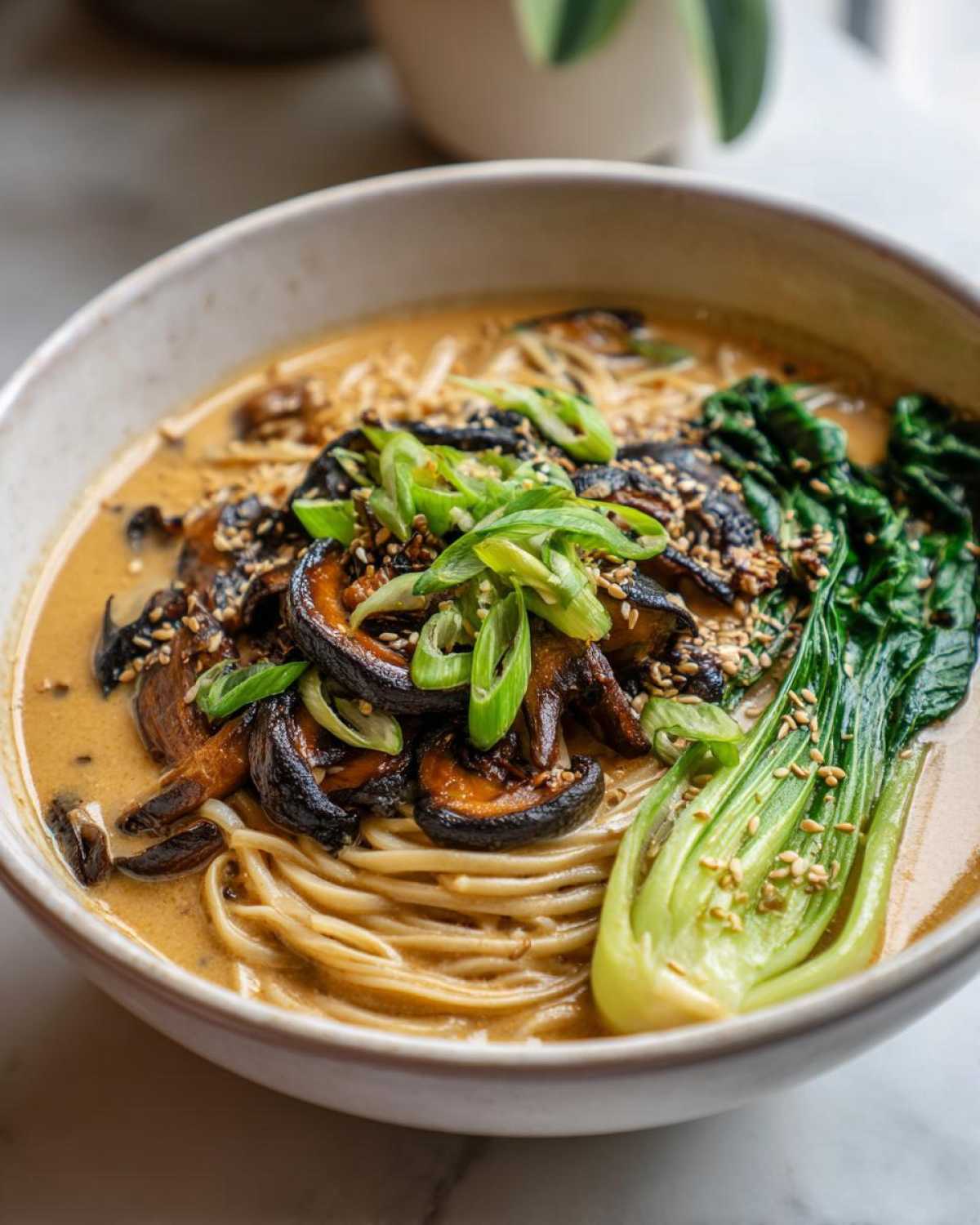 A close-up of a bowl of Vegan Creamy Miso Sesame Noodle Soup topped with shiitake mushrooms and bok choy.