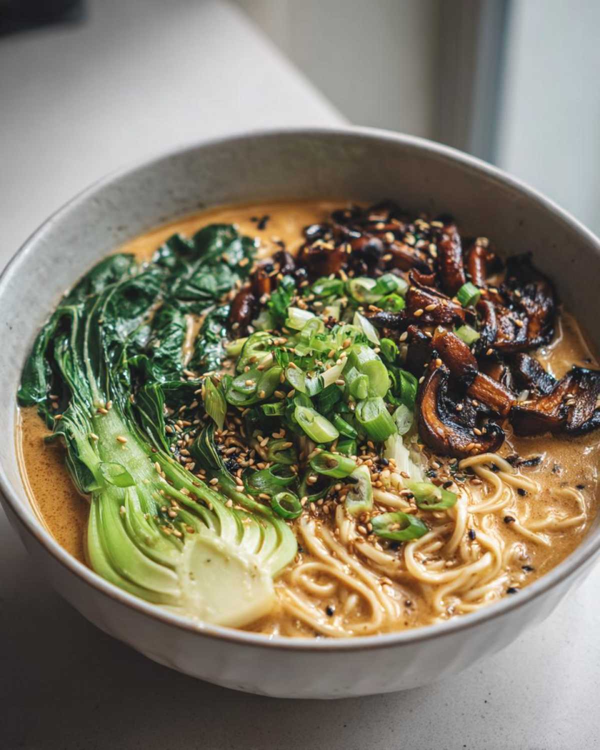 A close-up of a bowl of Vegan Creamy Miso Sesame Noodle Soup topped with bok choy, mushrooms, and scallions.