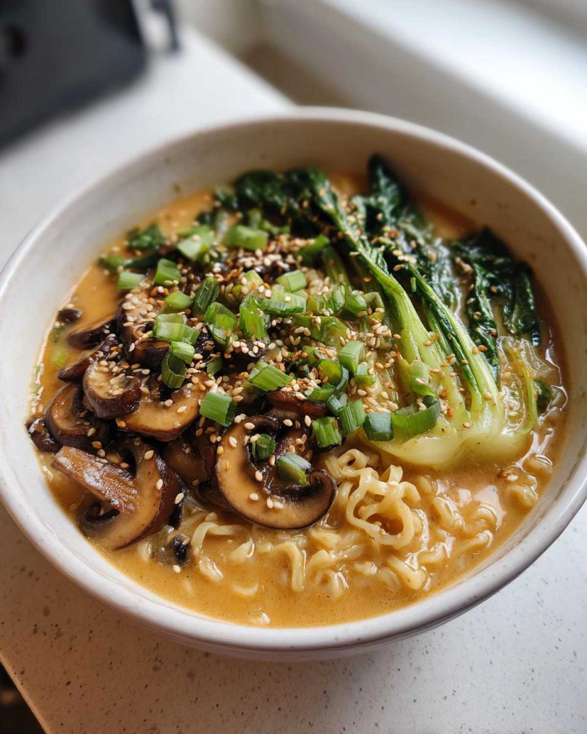 Close-up of a bowl of Vegan Creamy Miso Sesame Noodle Soup topped with mushrooms, bok choy, and green onions.