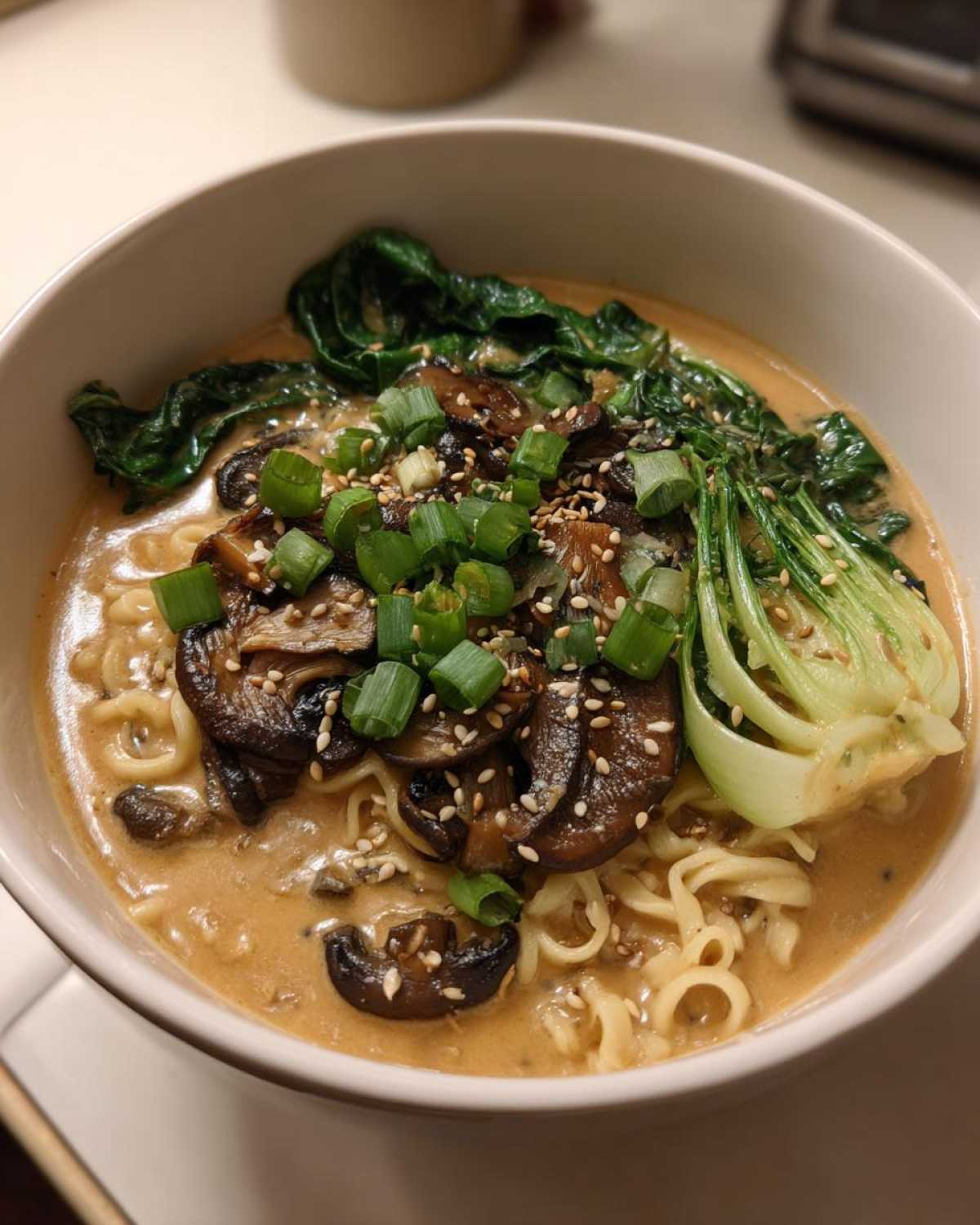 Close-up of a bowl of Vegan Creamy Miso Sesame Noodle Soup topped with mushrooms, bok choy, and green onions.