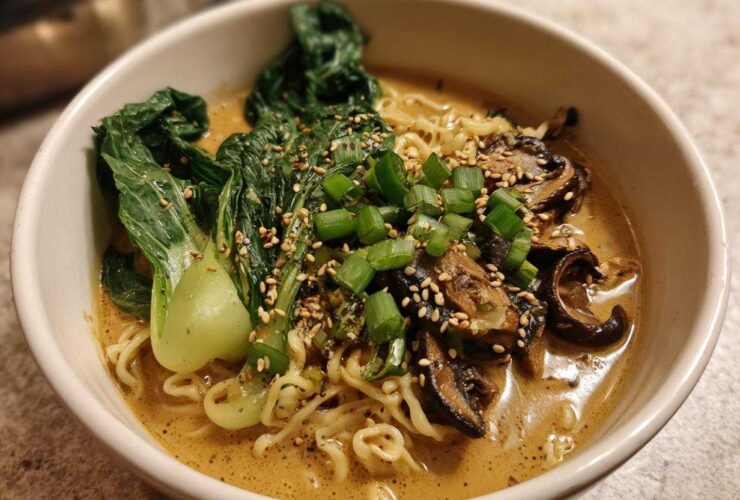 A close-up of a white bowl filled with Vegan Creamy Miso Sesame Noodle Soup, topped with bok choy, mushrooms, and scallions.