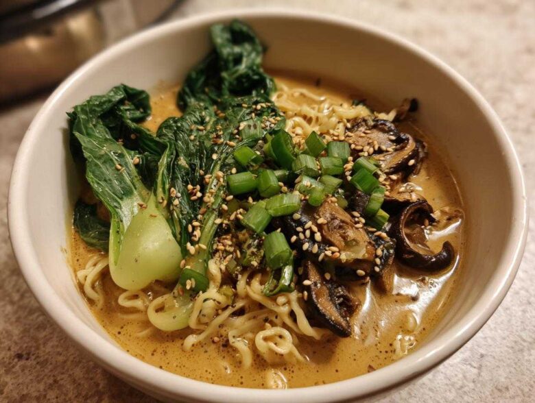 A close-up of a white bowl filled with Vegan Creamy Miso Sesame Noodle Soup, topped with bok choy, mushrooms, and scallions.