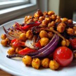 Close-up of seasoned, roasted chickpeas mixed with charred red onion, red pepper, and cherry tomatoes from the Vegan One-Pan Chickpea Shawarma Sheet Bake.