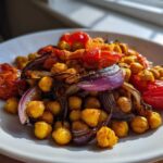 Close-up of roasted chickpeas, red onion wedges, and tomatoes seasoned for a Vegan One-Pan Chickpea Shawarma Sheet Bake.