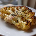 A thick slice of golden brown Baked Cauliflower Steaks, seasoned with herbs, served on a white plate.