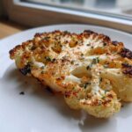 Close-up of a golden brown, perfectly Baked Cauliflower Steaks slice garnished with fresh green herbs.