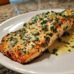 Close-up of a perfectly baked Garlic Butter Salmon fillet topped with melted butter, garlic, and fresh parsley.