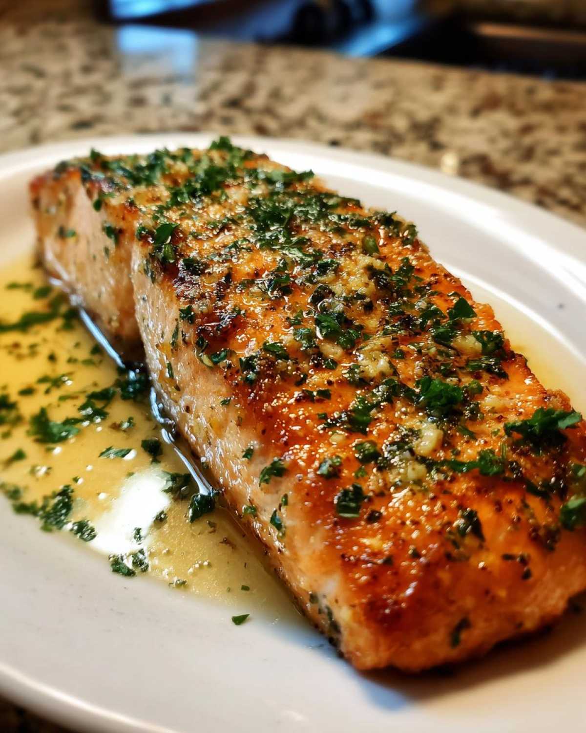 Close-up of a perfectly baked Garlic Butter Salmon fillet topped with minced garlic and fresh parsley, sitting in buttery sauce.
