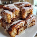 A stack of gooey Banana Bread Batter Cinnamon Buns drizzled generously with white icing.