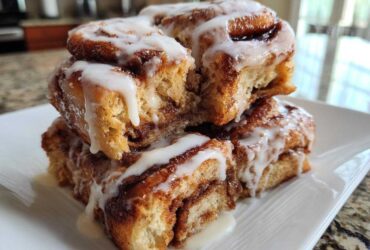A stack of gooey Banana Bread Batter Cinnamon Buns drizzled generously with white icing.