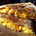 Two halves of a golden-brown quesadilla filled with fluffy scrambled eggs and melted cheddar cheese, showcasing the Cheddar Eggs Quesadillas.