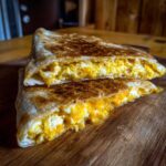 Two halves of a toasted tortilla filled with fluffy scrambled eggs and melted cheddar cheese, forming delicious Cheddar Eggs Quesadillas.