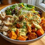 Close-up of a Chicken Sweet Potato Power Bowl featuring roasted sweet potatoes, shredded chicken, greens, and a generous tahini drizzle.