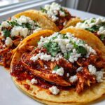 A plate of several vibrant Chicken Tinga Tacos Chipotle topped generously with crumbled white cheese and fresh cilantro.