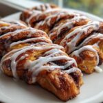 Close-up of freshly baked Cinnamon Roll Bread Twists drizzled generously with white icing on a white plate.