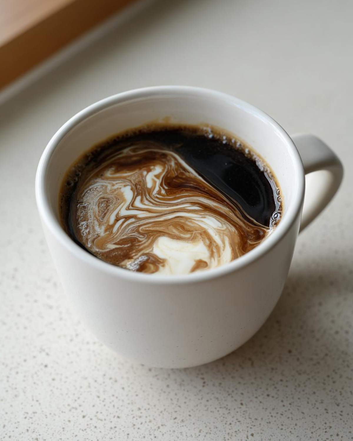 Close-up of dark coffee in a white mug with cream swirling into it, illustrating Vanilla Infusion for Quick Mornings.