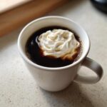 Close-up of dark coffee in a white mug topped with a dollop of whipped cream, illustrating Vanilla Infusion for Quick Mornings.