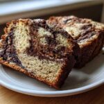 Two slices of Cream Cheese Cinnamon Swirl Banana Bread showing a rich swirl pattern, served on a small white plate.