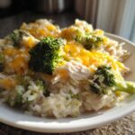 A close-up of Crockpot Broccoli Cheddar Chicken and Rice served on a white plate, topped with melted cheese.