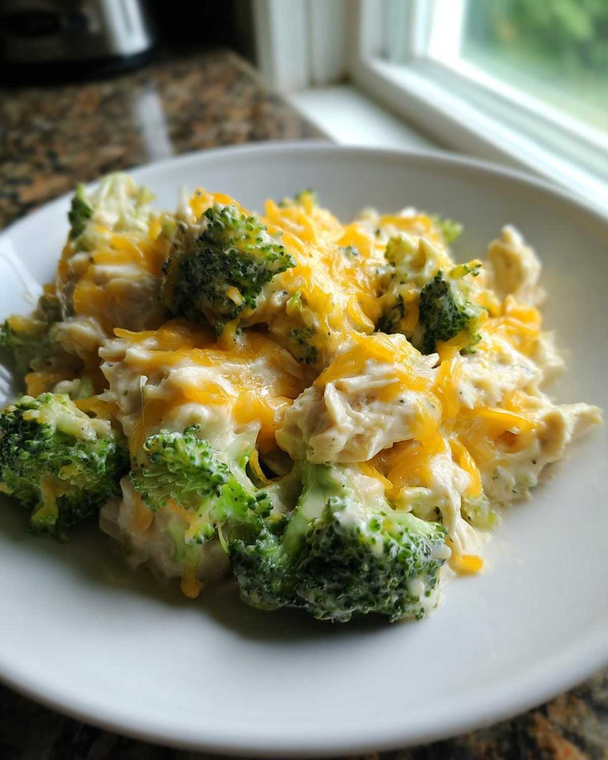 A close-up serving of Crockpot Broccoli Cheddar Chicken and Rice topped with melted orange cheddar cheese.