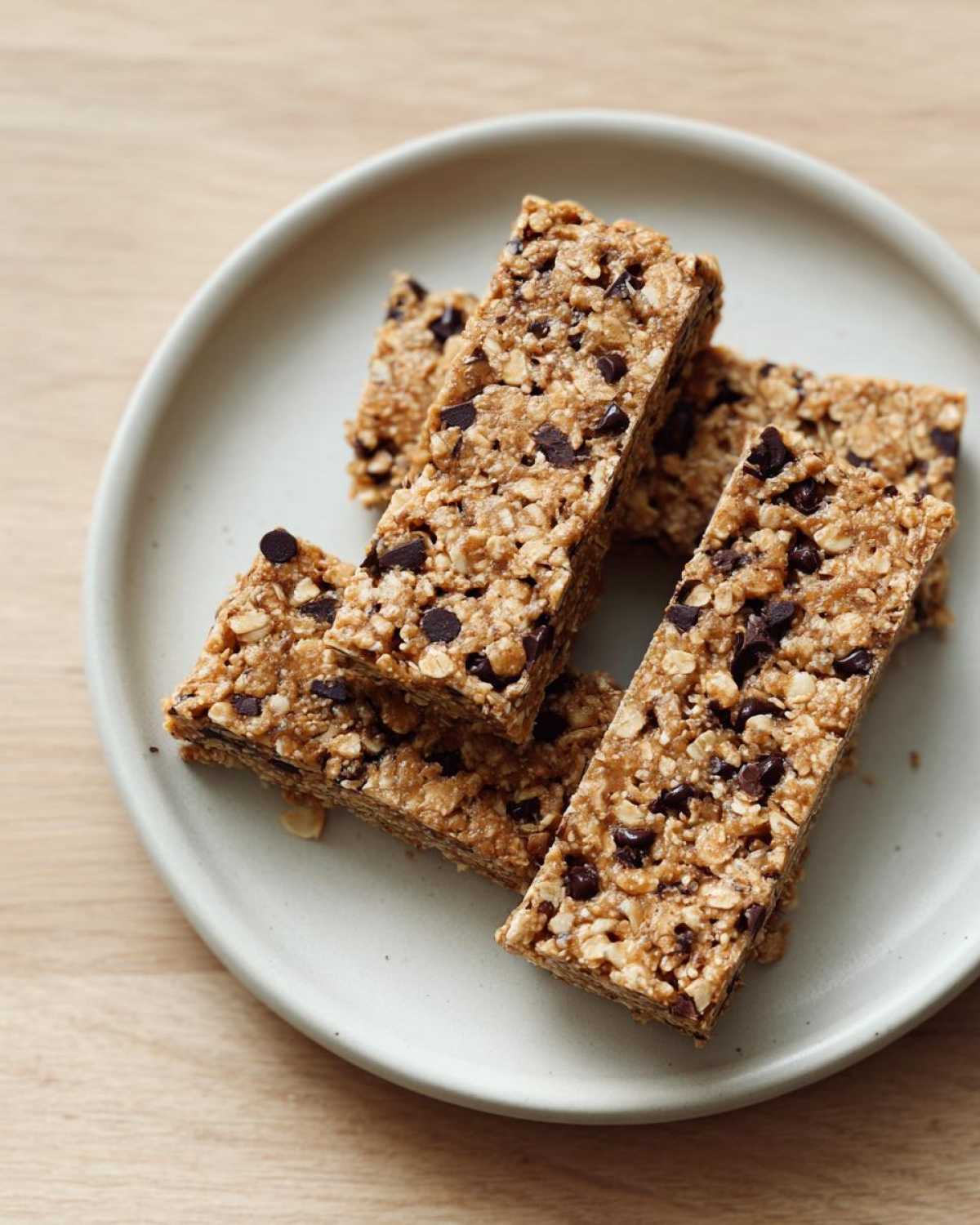 Several homemade high-protein snack bars packed with oats and mini chocolate chips stacked on a light gray plate.