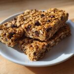 Four homemade high-protein snack bars packed with oats and chocolate chips stacked on a small white plate.