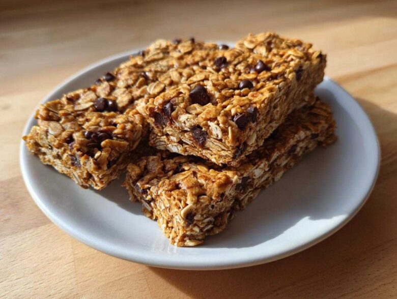 Four homemade high-protein snack bars packed with oats and chocolate chips stacked on a small white plate.