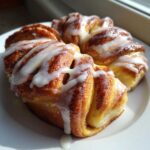 Close-up of freshly baked Cinnamon Roll Bread Twists drizzled generously with white icing on a white plate.