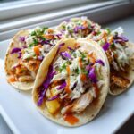 Four Hawaiian Chicken Tacos filled with shredded chicken, pineapple, purple cabbage slaw, and drizzled with orange sauce.