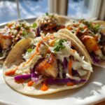 Four delicious Hawaiian Chicken Tacos filled with grilled chicken, colorful slaw, and drizzled with sauce, served on a white plate.