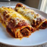 Two cheesy, saucy High Protein Chicken Enchiladas filled with shredded chicken, served on a white plate.